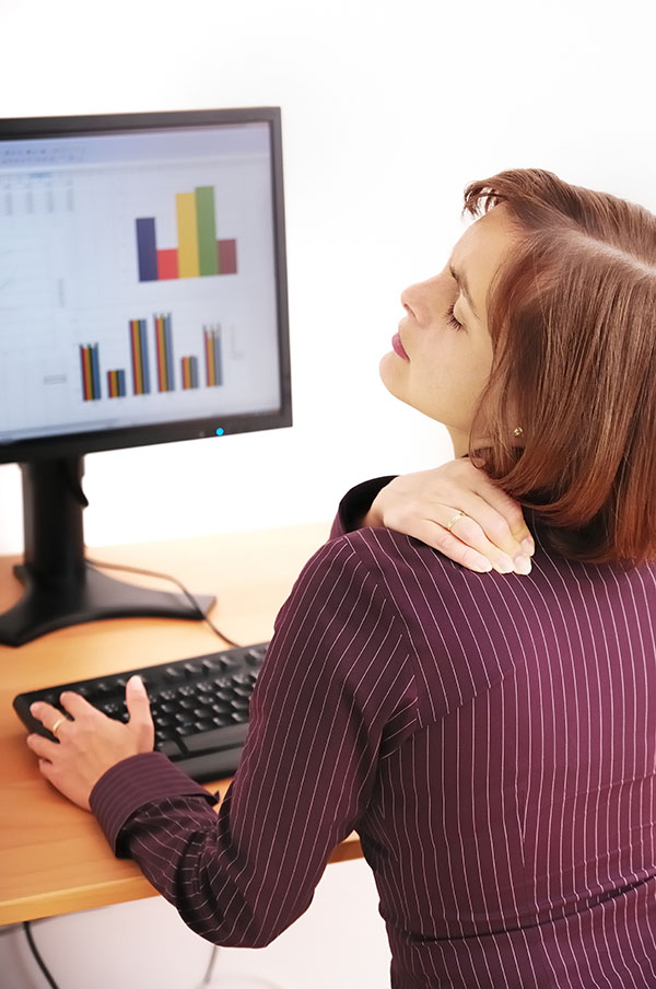 Mujer con dolor cervical trabajando en ordenador oficina cervicalgia
